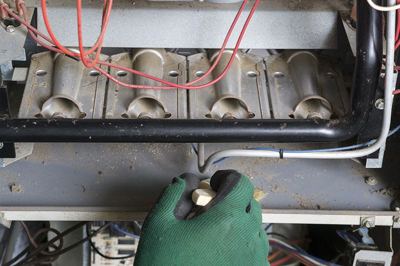 Image of someone working on a furnace with green gloves. When Should You Replace Your Furnace?