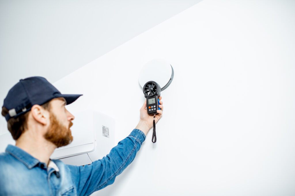 Handyman checking the speed of air ventilation with measuring tool on the white wall background